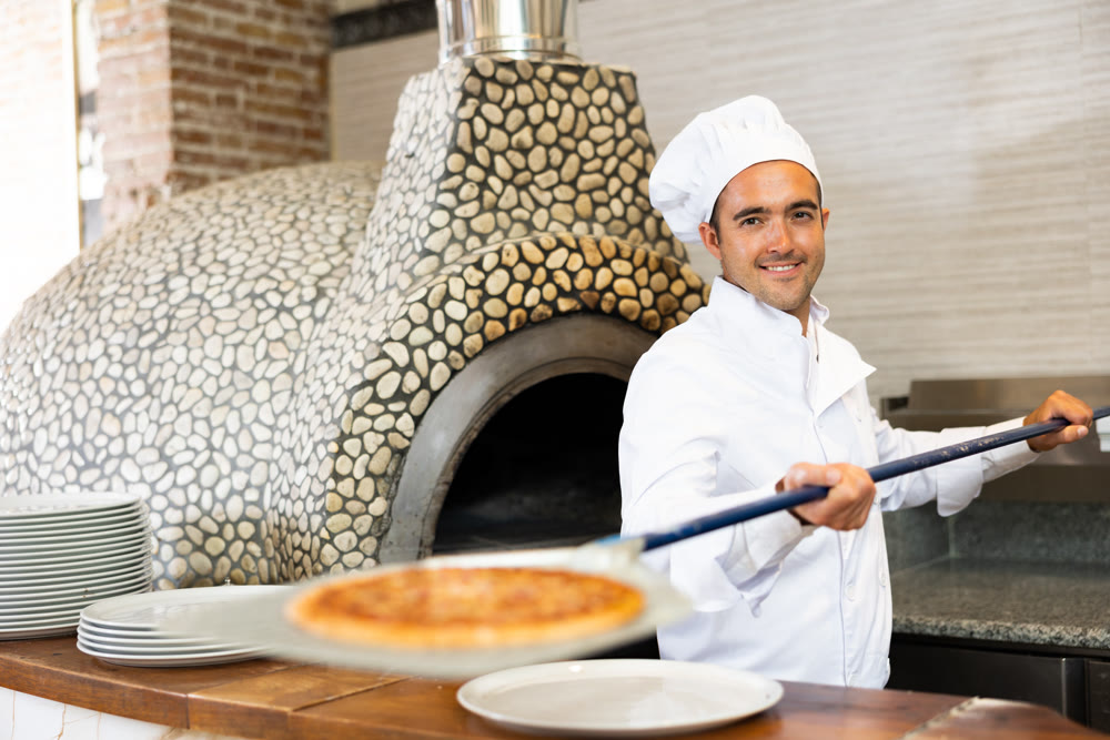 Skilled man chef preparing pizza in restaurant