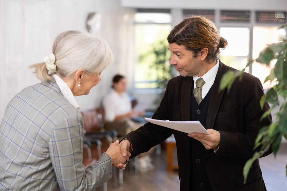 Adult man and elderly woman shaking hands in office