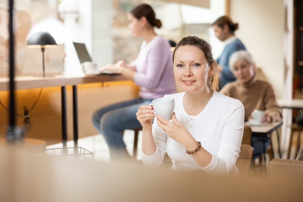 Dreamy woman sitting with cup of coffee in cozy cafe