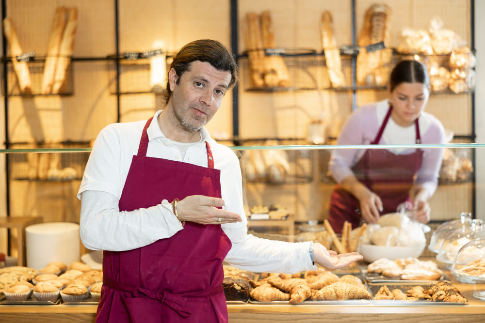Interested successful baker in maroon apron inviting to bakeshop