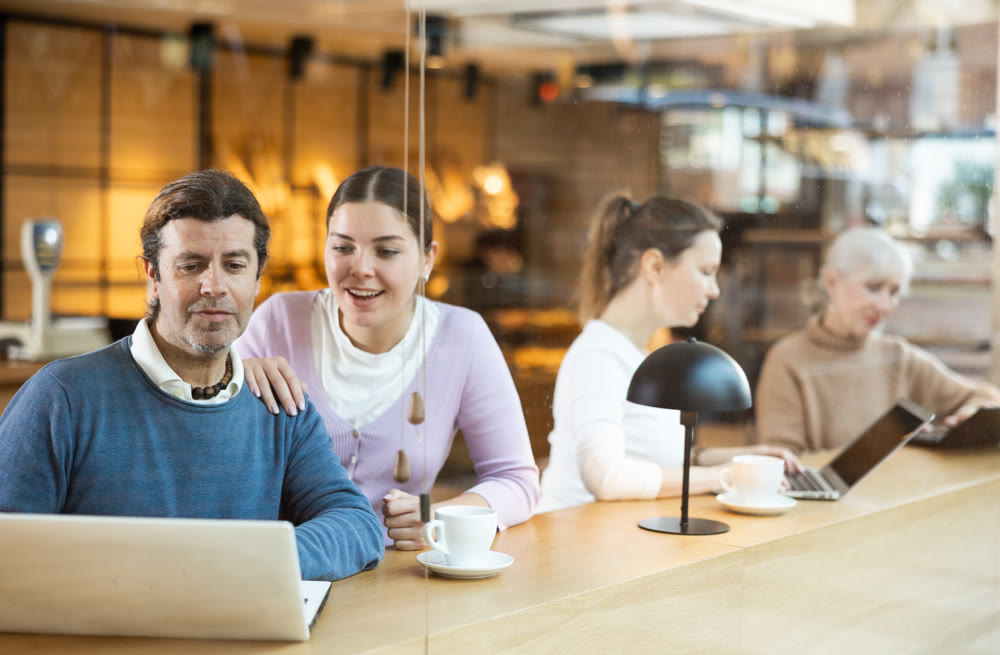 Confident male and female cafe customer enjoying coffee while working on laptop