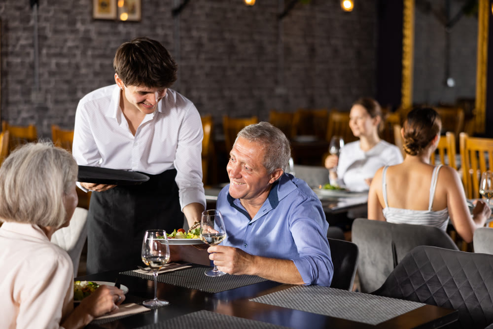 Restaurateur guy serves customers elderly spouses plate with dinner order