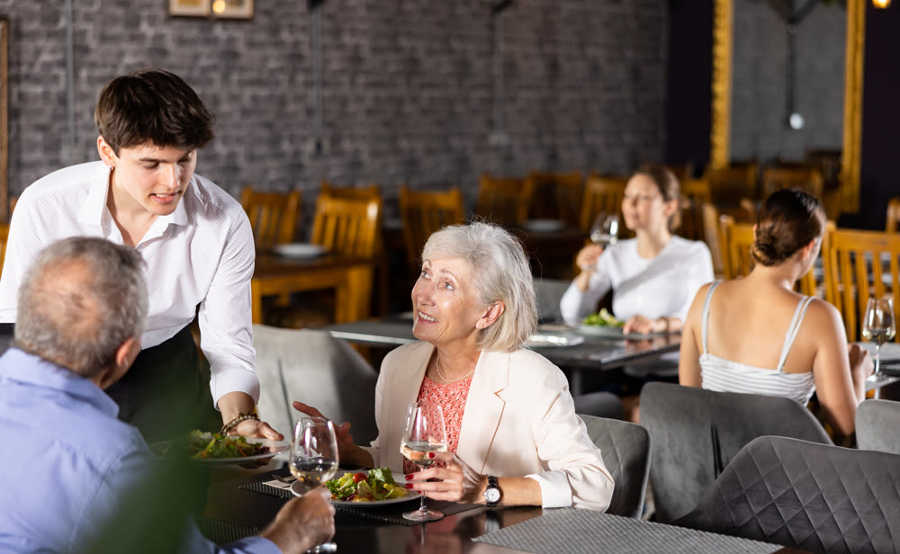 Restaurateur guy serves customers elderly spouses plate with dinner order