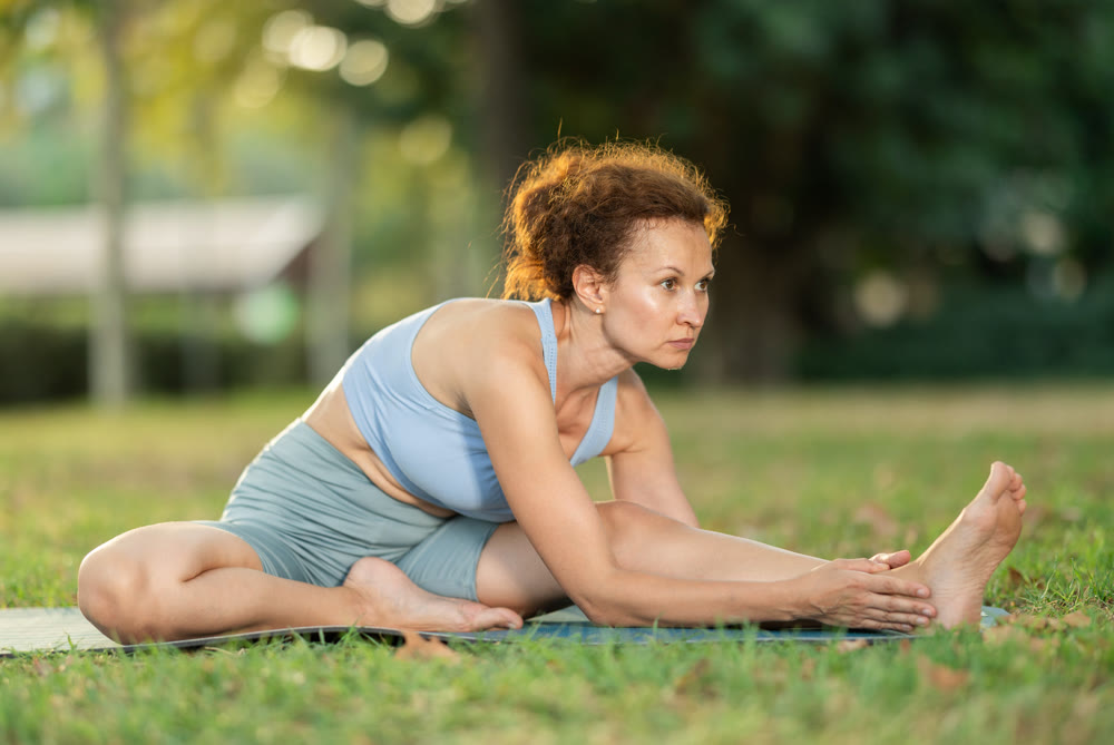 Woman practicing hatha yoga in garden, stretching in an asymmetrical seated asana Parivritta Janu Sirsasana