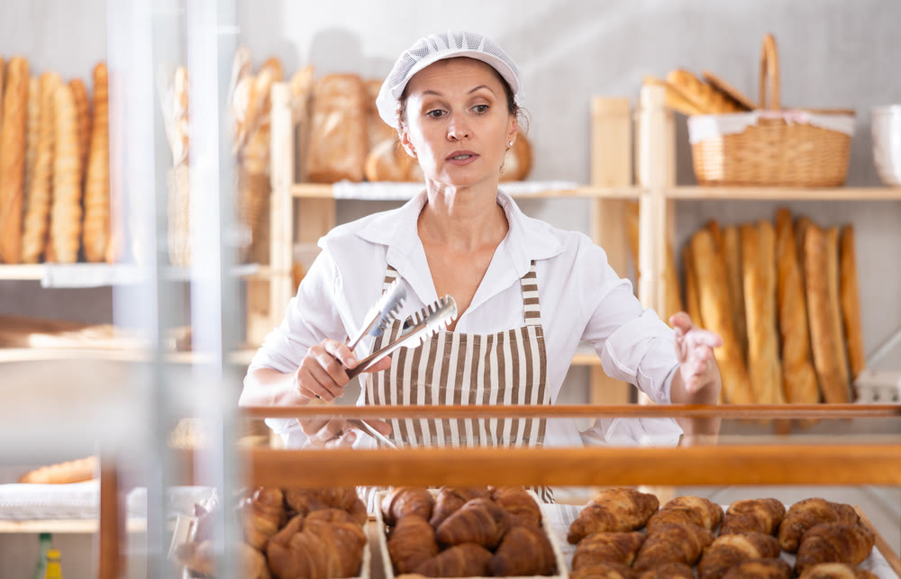 Girl baker worker sell croissants, shows different crescent rolls.