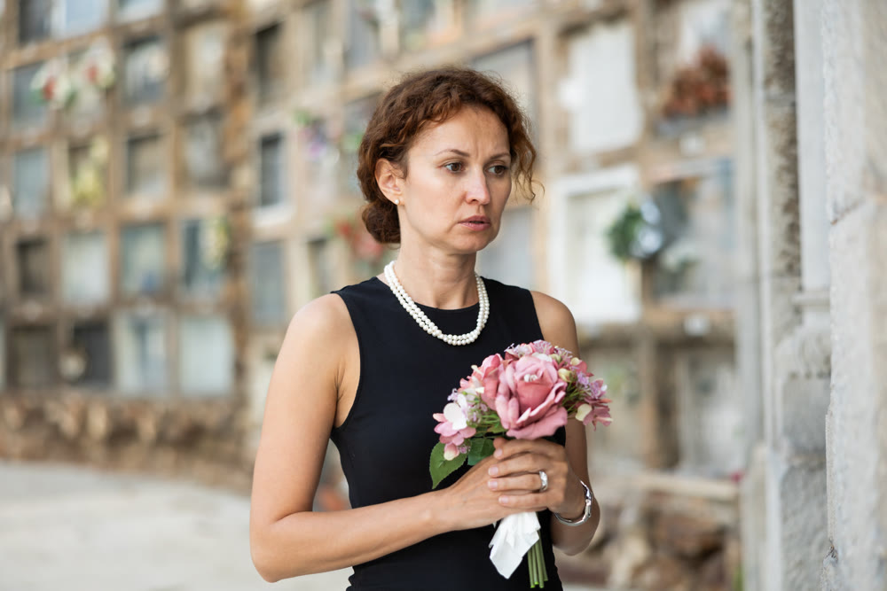 Woman in black mourning dress standing with flowers near columbarium