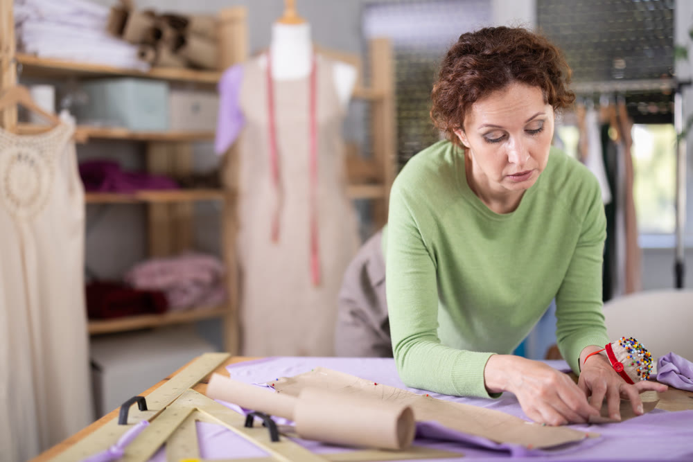 Woman tailor applies paper pattern to fabric to check