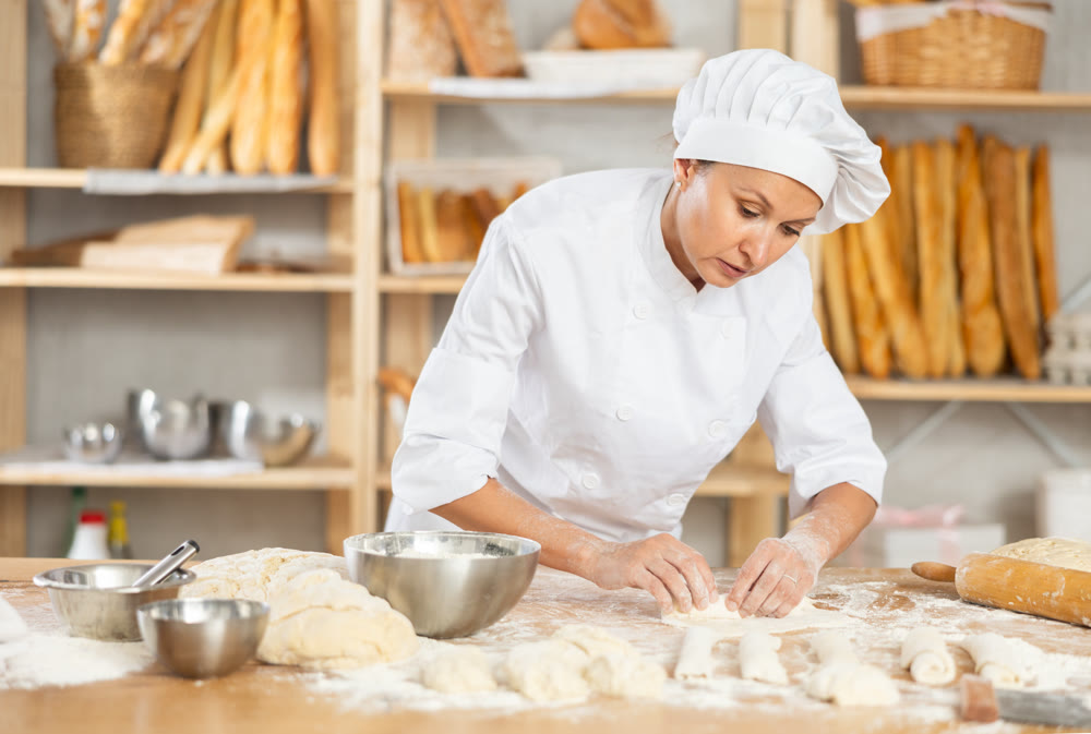 Female employee cooks croissants, rolls dough into tube, forms muffin from raw dough material
