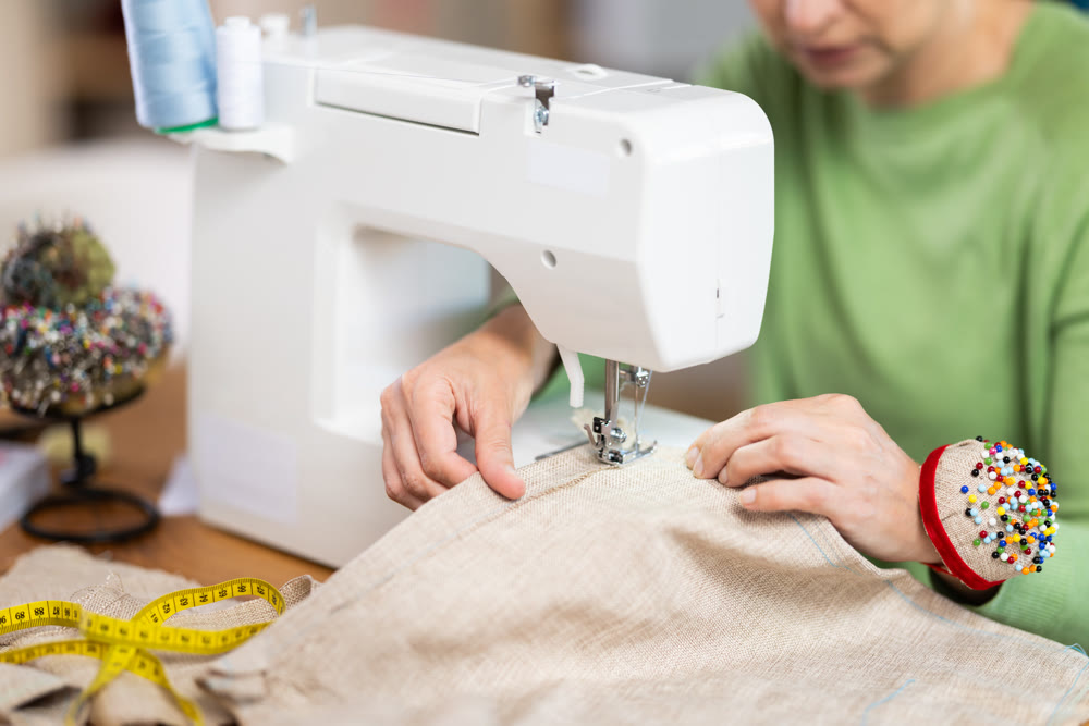 Hands of seamstress sewing linen fabric on machine