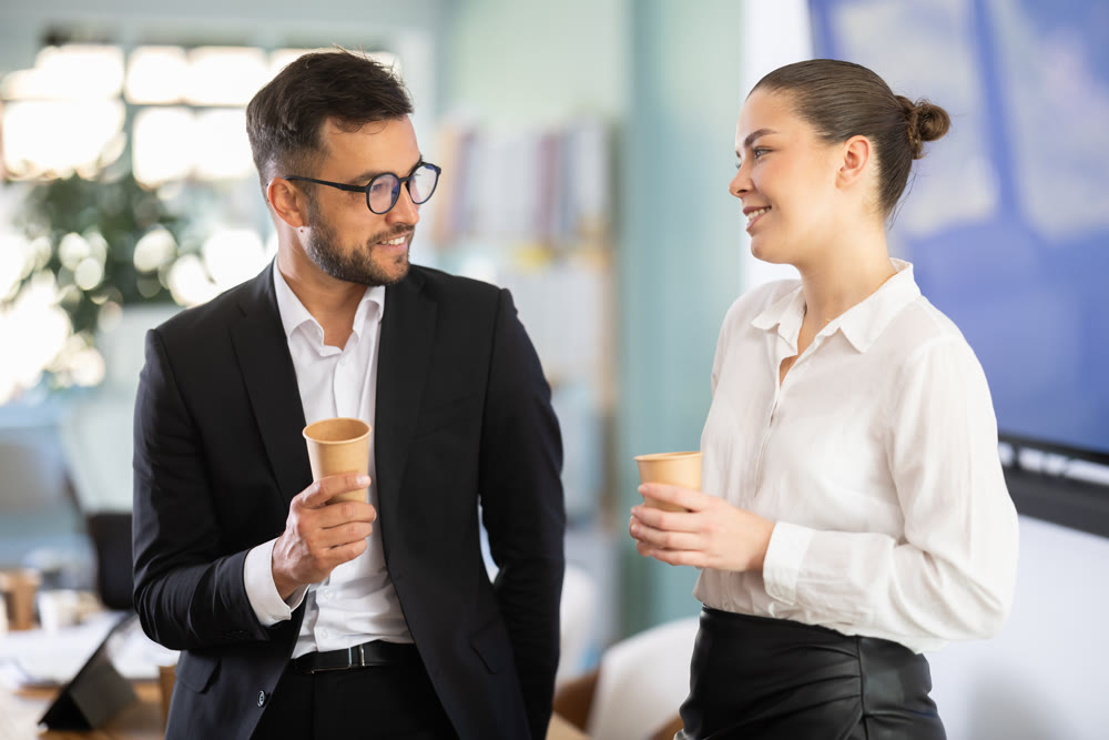 Man and woman talking, laughing and joking with cup of coffee in hands, coffee break time