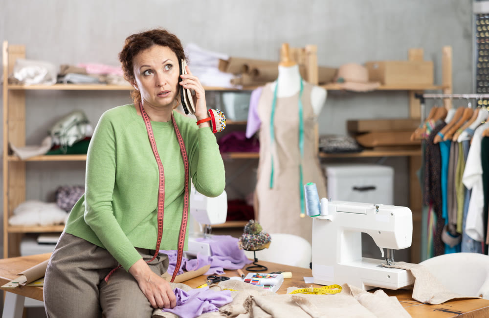 Female tailor talking on phone in sewing workshop