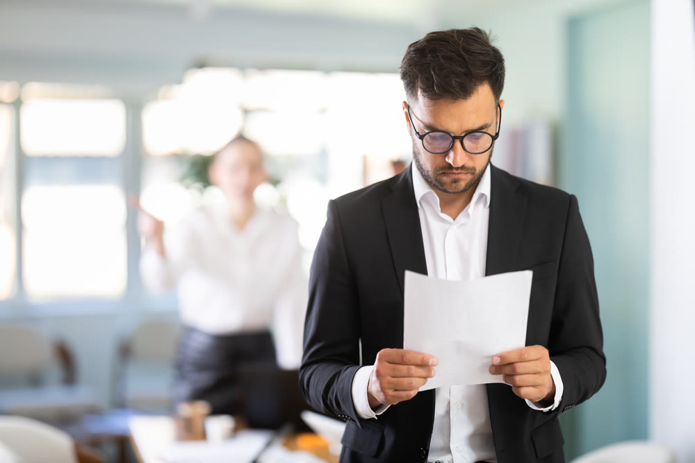 Sad man standing in office, he holding resignation papers