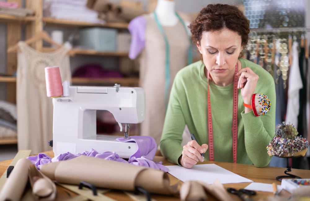 Sad female dressmaker sitting over blank sheet of paper in sewing studio
