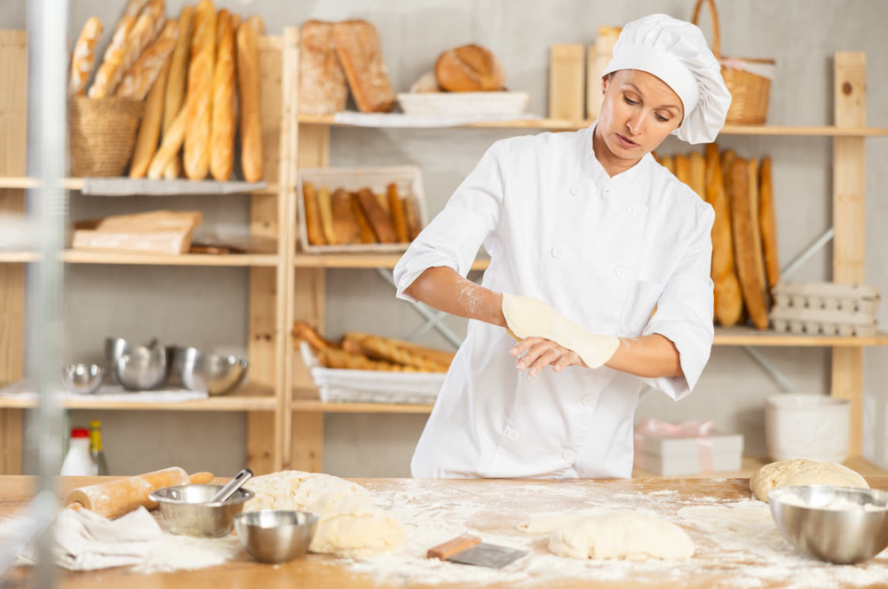 Professional female baker preparing pizza dough in bakery
