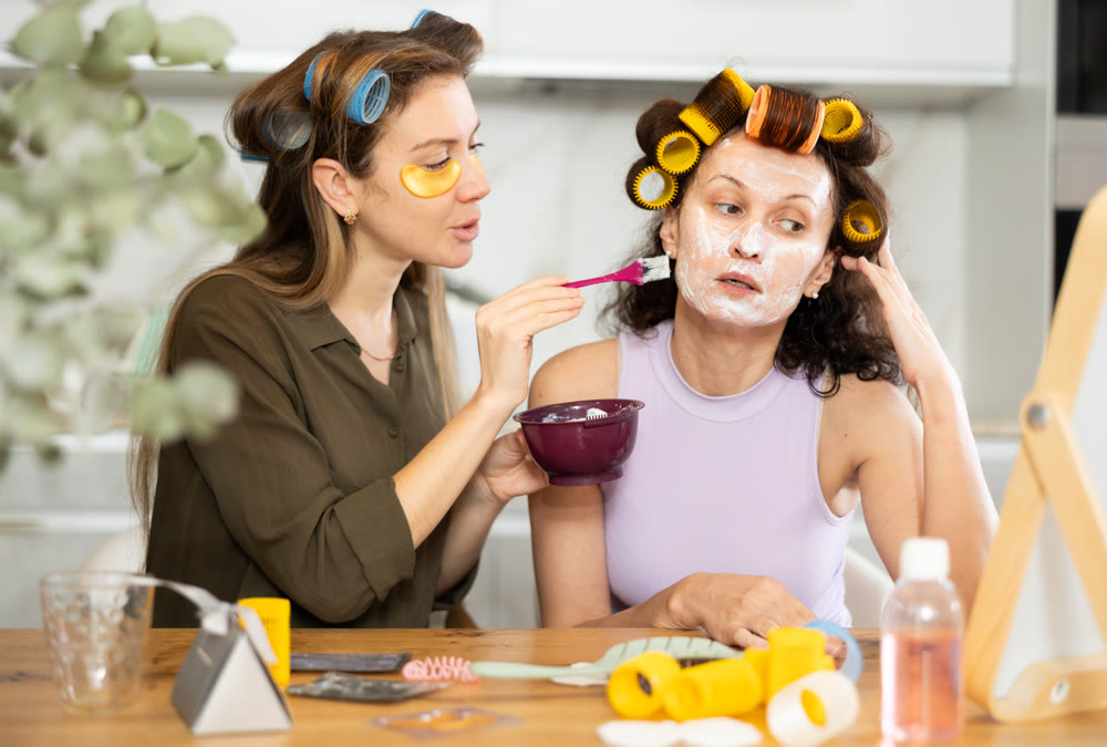 Relaxed female friends applying facial mask to each other at home