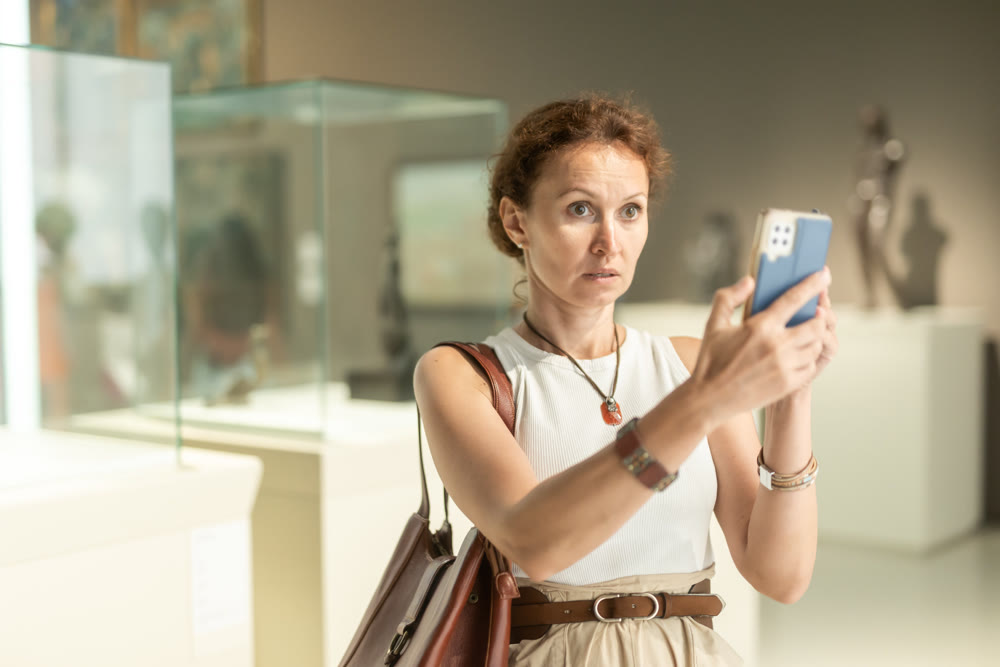 Attractive young woman in casual clothing photographing painting in museum