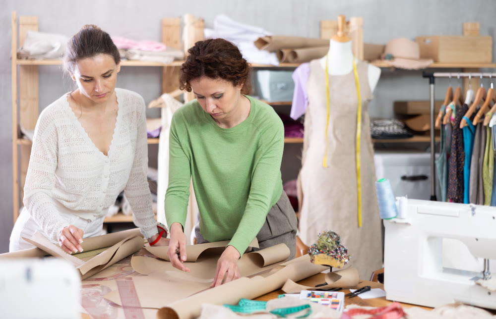 Two women tailor draw dress pattern of product on paper