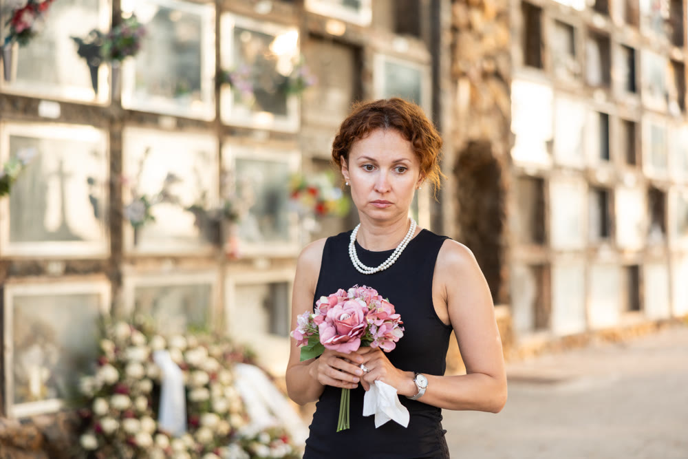 Woman in black mourning dress standing with flowers near columbarium