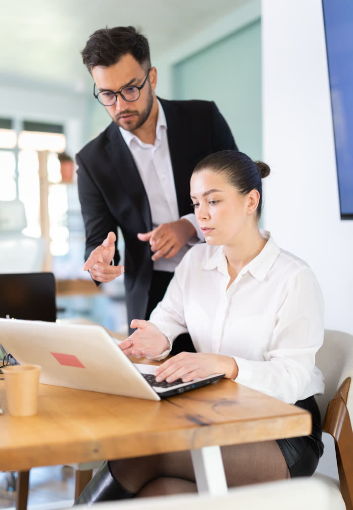 IT specialist man helps a young female employee work on a laptop