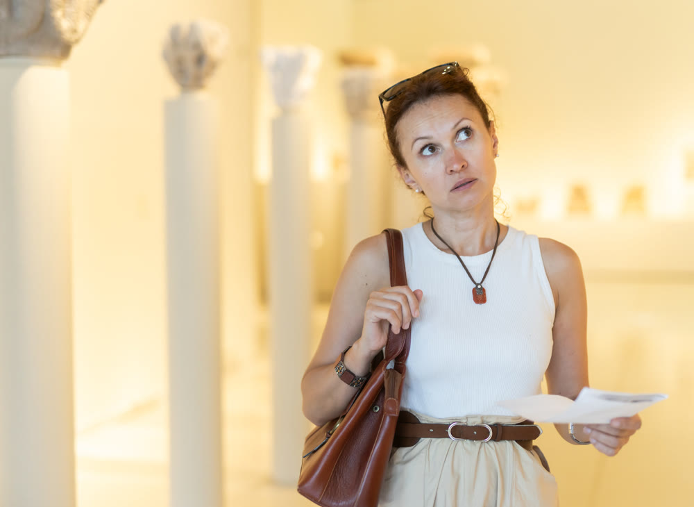 Focused woman visitor with booklet in her hands examines exhibit standing in art gallery