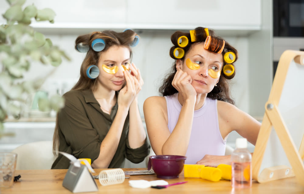Two women curl their hair with curlers and use patches