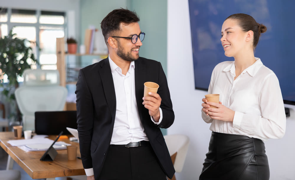 Two office workers drink coffee and chat during work break