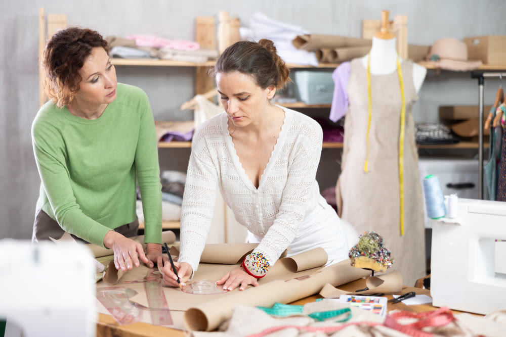 Female seamstresses drafting clothing pattern on paper in sewing workshop