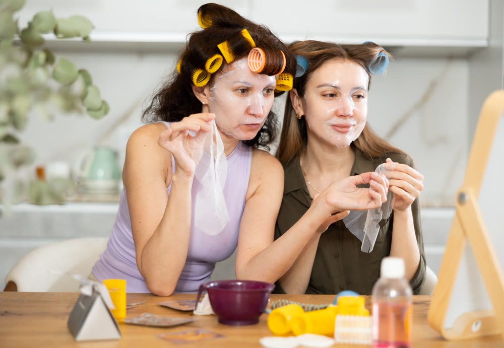 Two adult besties applying facial mask at home together
