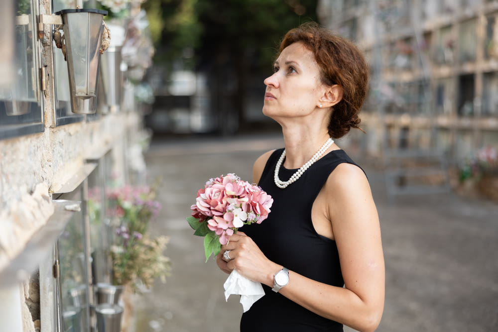Woman standing with flowers in front of memorial wall in cemetery