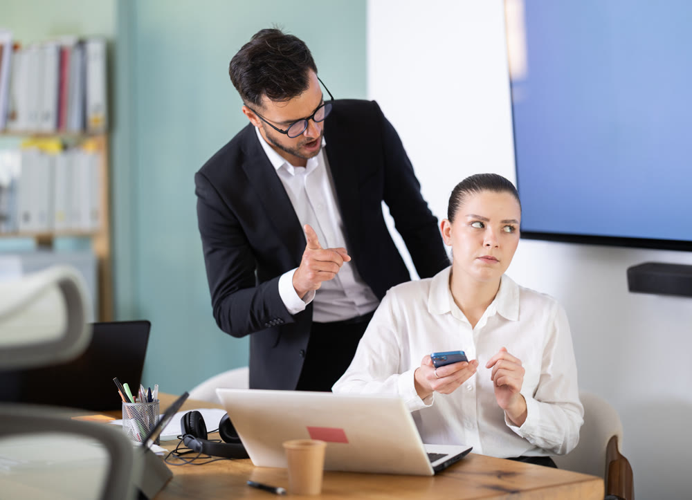 boss scolds at a woman who sits at the table and scrolls through social networks