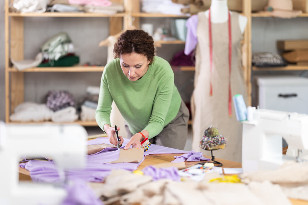 Female dressmaker cutting fabric with scissors while working in sewing workshop