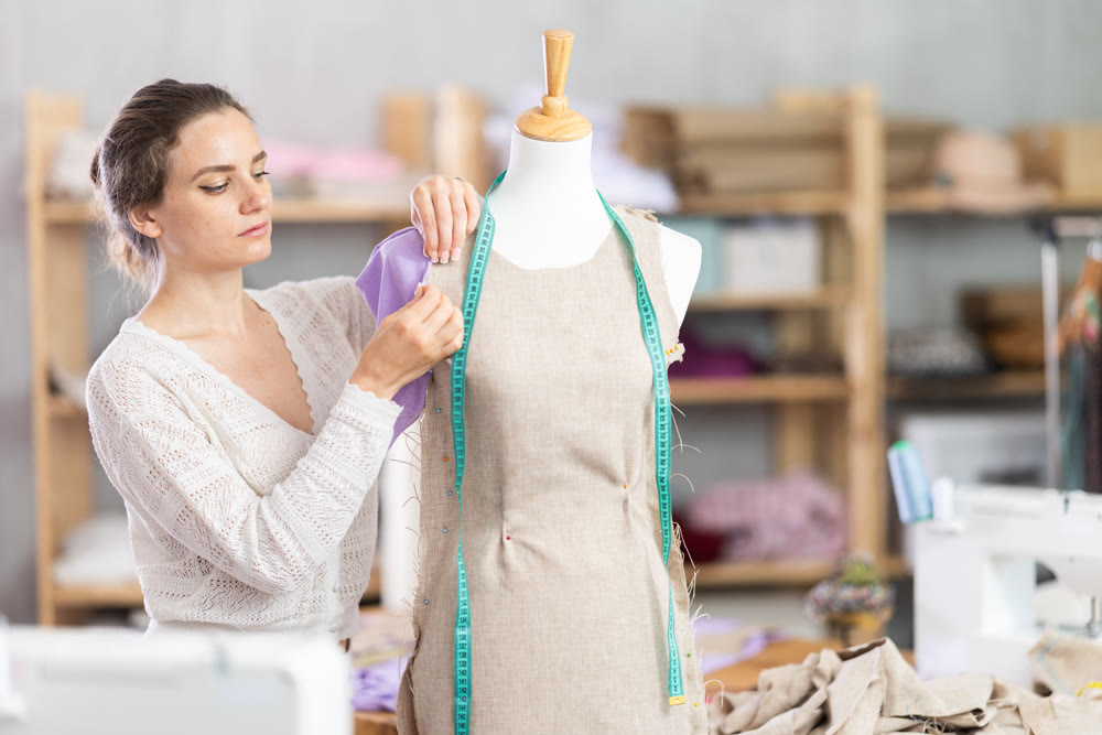 Female tailor sews new dress on a mannequin in sewing studio