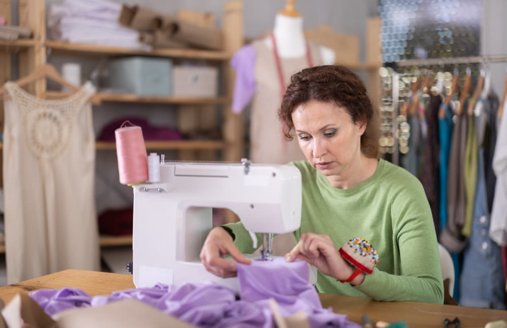 Working in sewing workshop - female dressmaker working at sewing machine making stitches on fabric