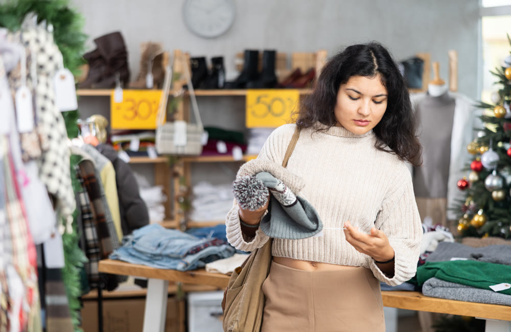 Female shopper selects warm hat in fashionable clothing boutique