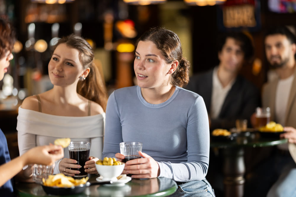 Three happy young female friends laughing and spending time together in sports bar