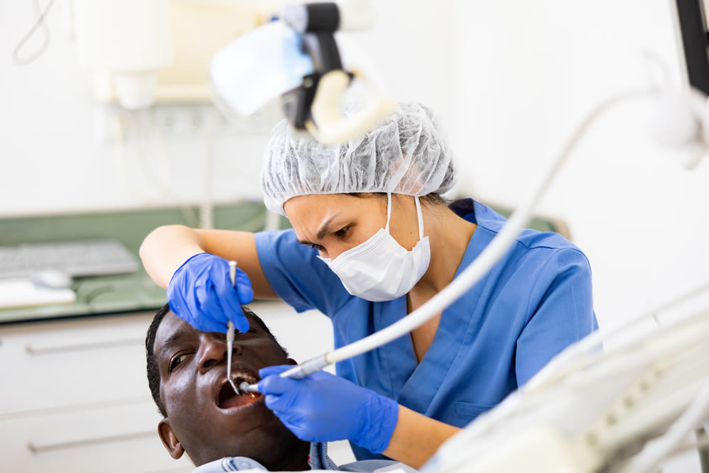 Female dentist performing teeth treatment to adult man at clinic