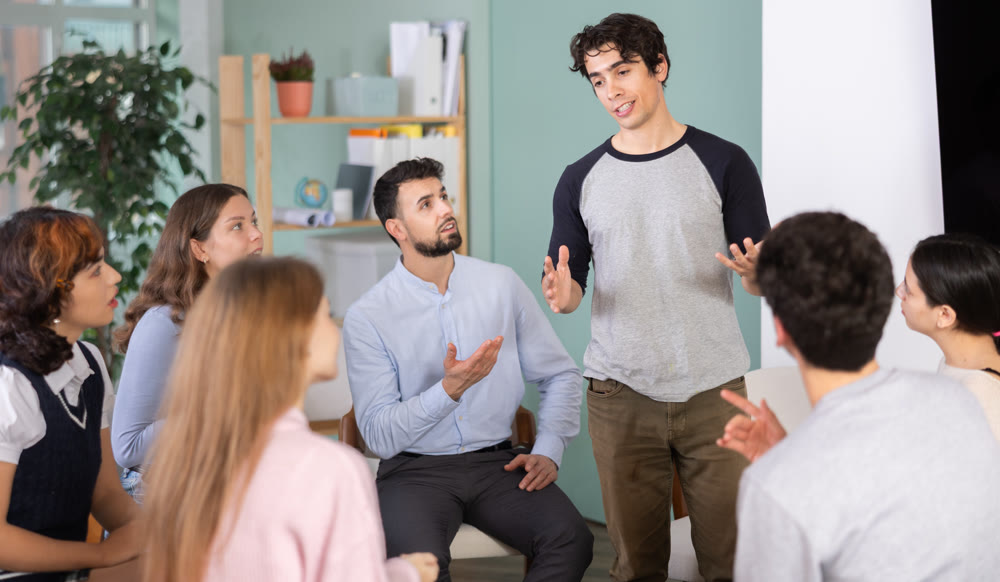 Guys and girls are sitting in circle and listening to one of their guy friend classmate