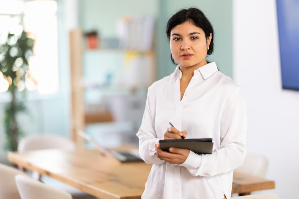Portrait of friendly young woman with tablet in office or training room.