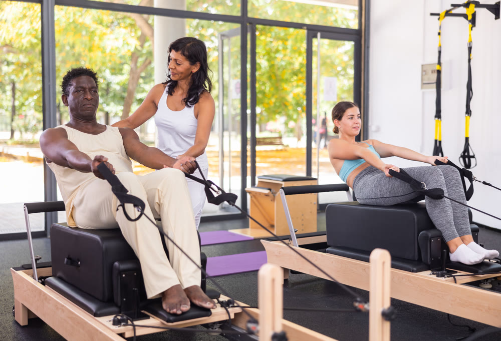 Female pilates trainer helping pilates man during training