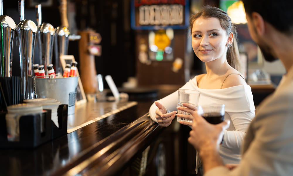 Young woman drinking beer and chatting with man at bar