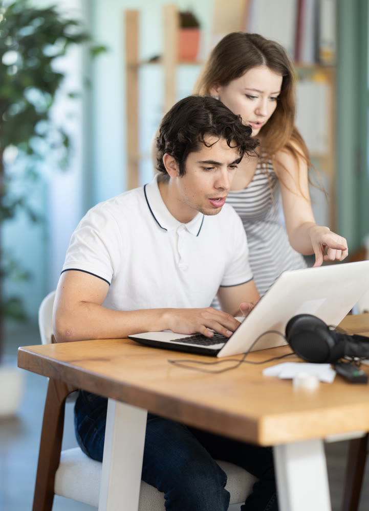 Young woman helping young male colleague work on laptop