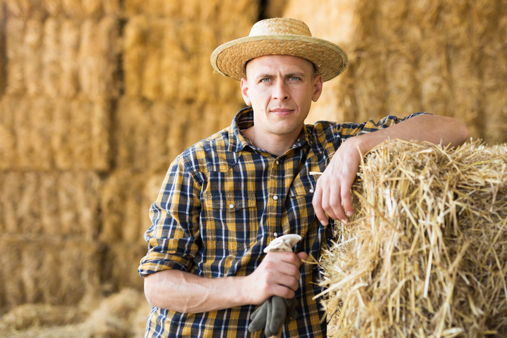 Confident male farmer posing near straw stack