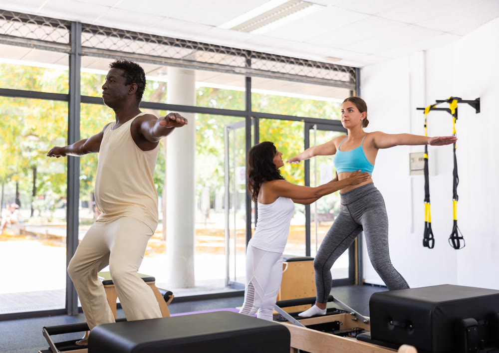 Man and woman doing exercises in pilates gym with man instructor
