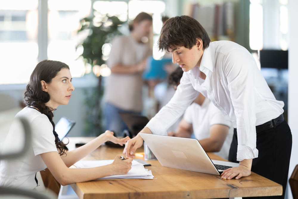 Young man showing place to sign on document to young woman filling