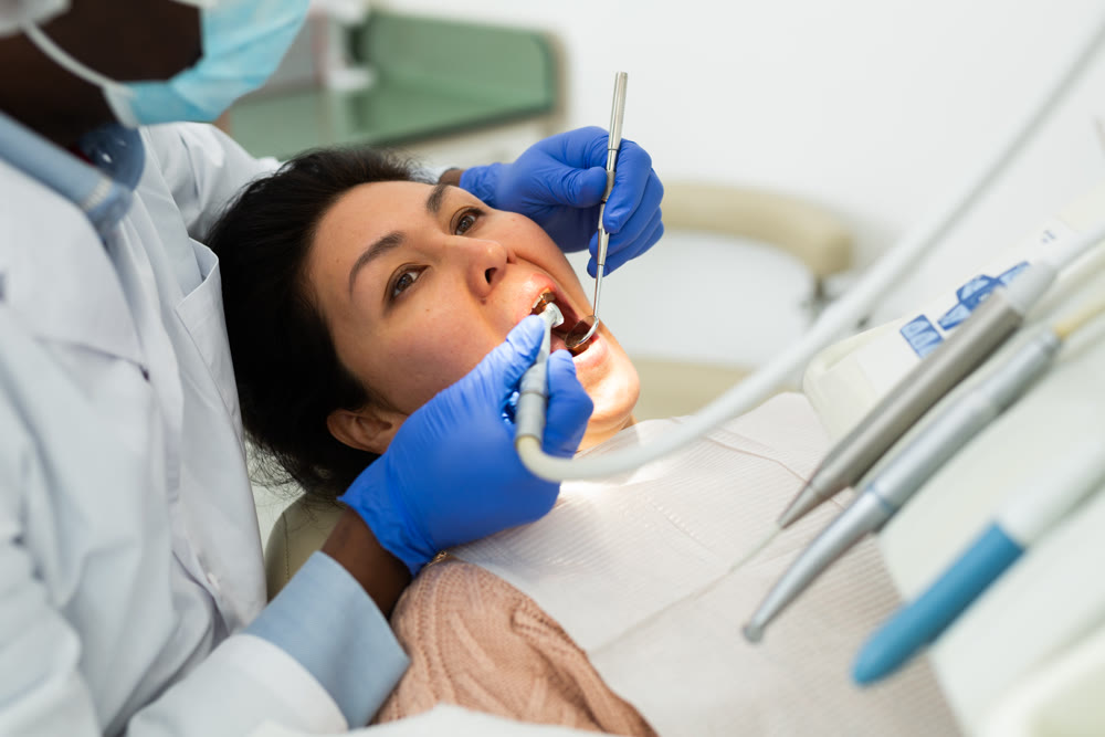 African american dentist is treating female patient which is sitting in chair