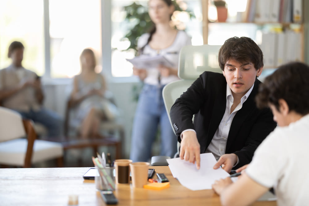 Man bank employee sits at desk and communicates with unrecognizable male client.