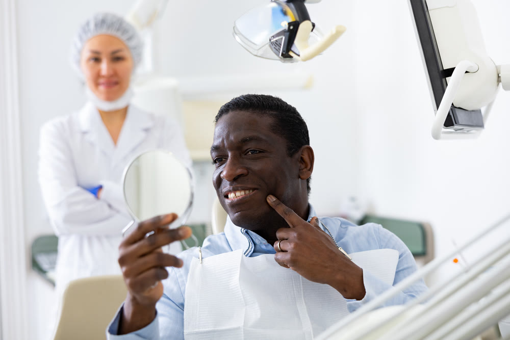 Man looking in mirror to evaluate results of dental restoration procedure