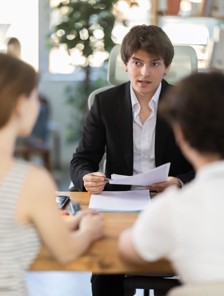 Man bank employee sits at desk and communicates with unrecognizable couple of clients