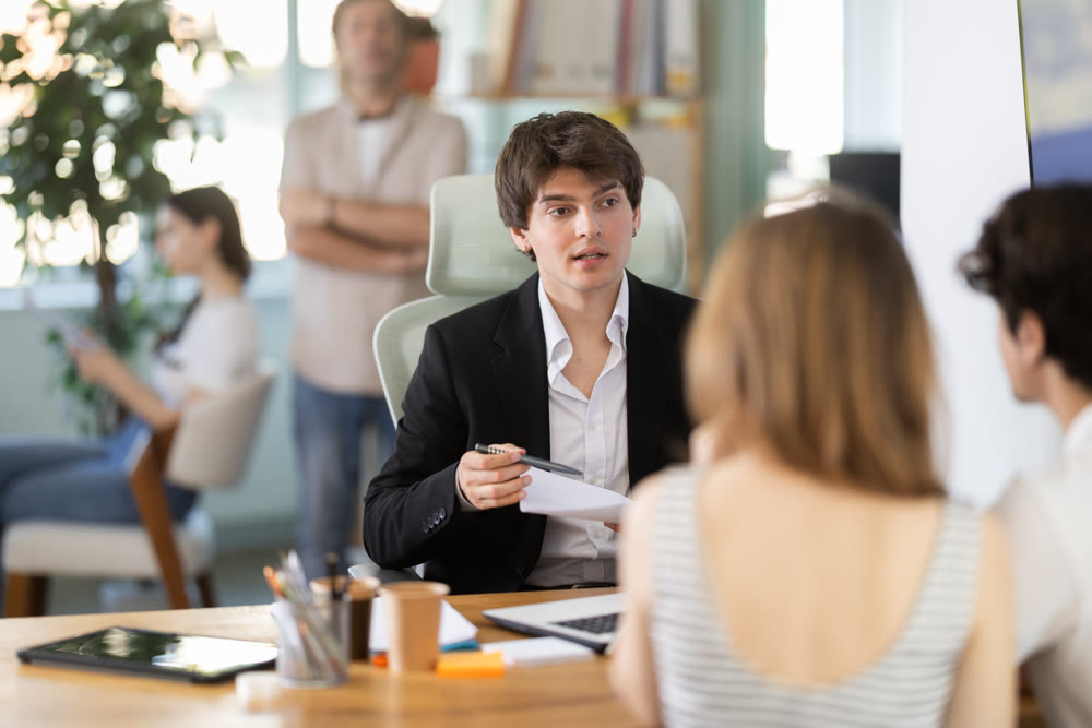Man bank employee sits at desk and communicates with unrecognizable couple of clients