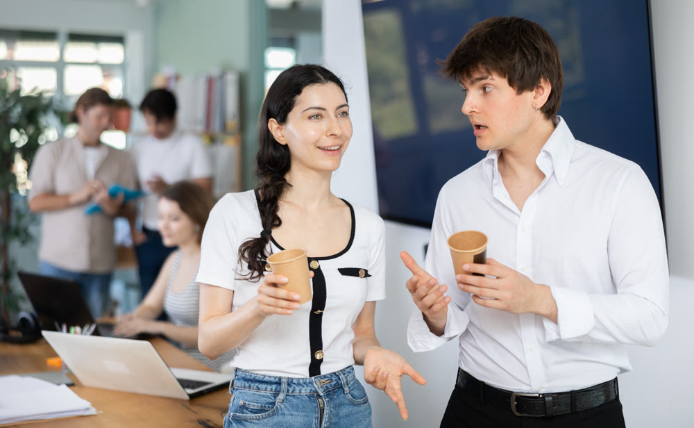 Young man and woman colleagues drinking coffee in office
